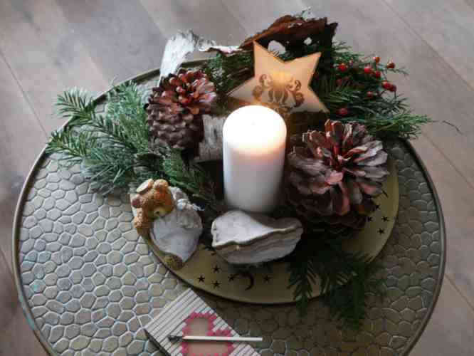 Adventskerze mit Zapfen, Tanne, Figur und Stern auf einem Tisch.