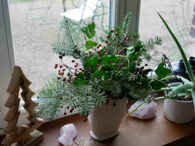 Vase mit Tannengrün und Früchten auf einer Fensterbank.