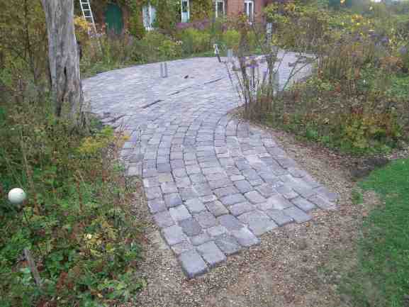 Zum Garten und Rasen auslaufende Pflasterfläche..