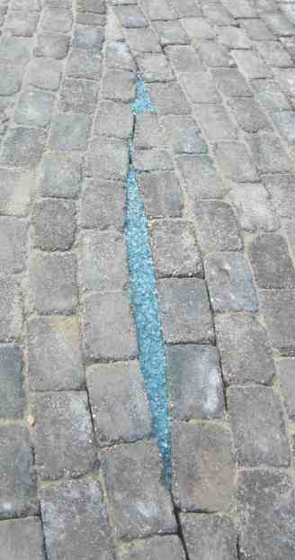 Hellblauer Glassplitt in länglichem Spalt inmitten des Pflasters.