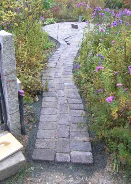 Gepflasterter Weg zwischen Blumenbeeten.